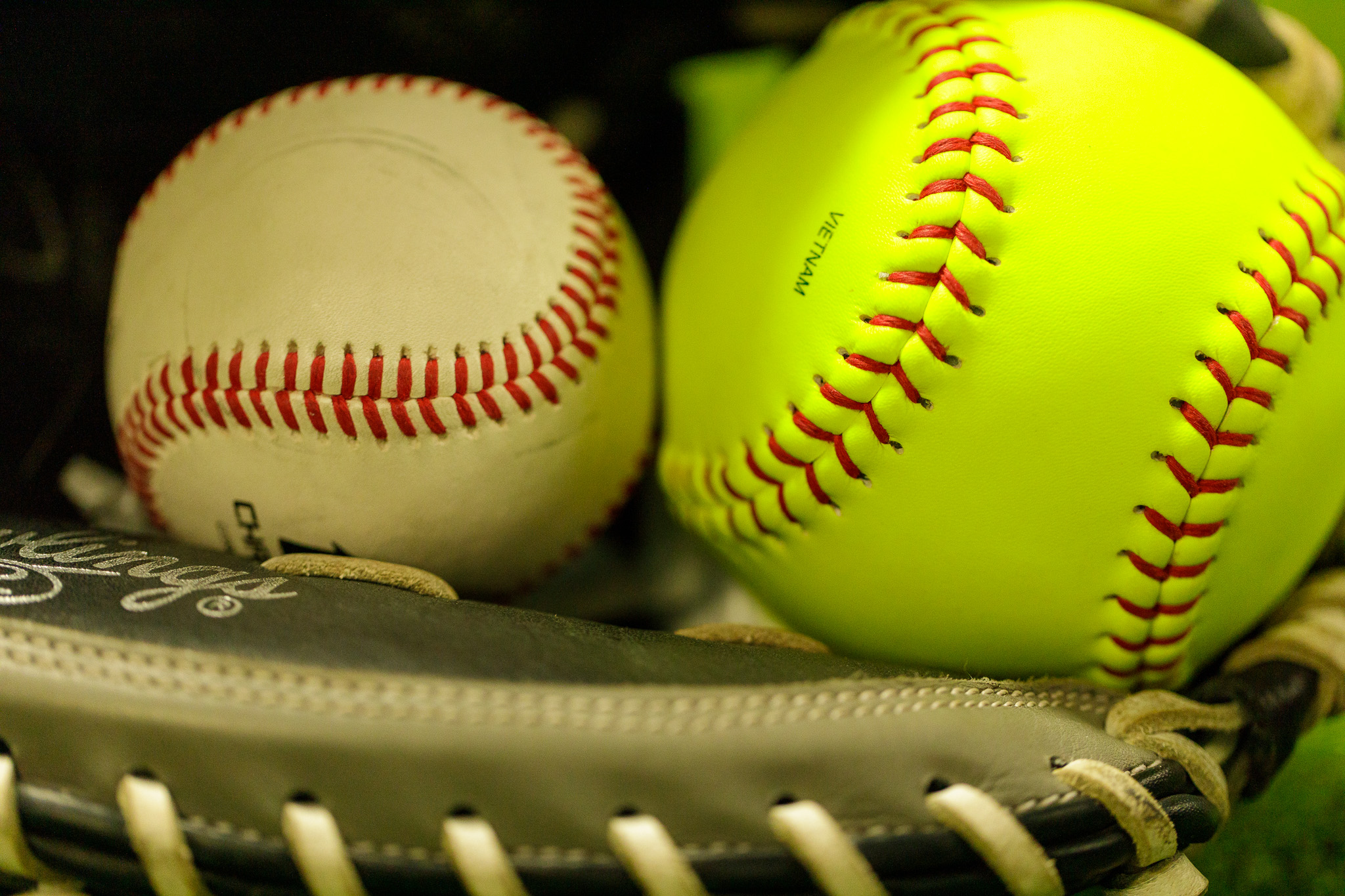 Baseball and softball side by side in a glove
